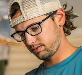 Man in a baseball cap wearing dark rectangular glasses